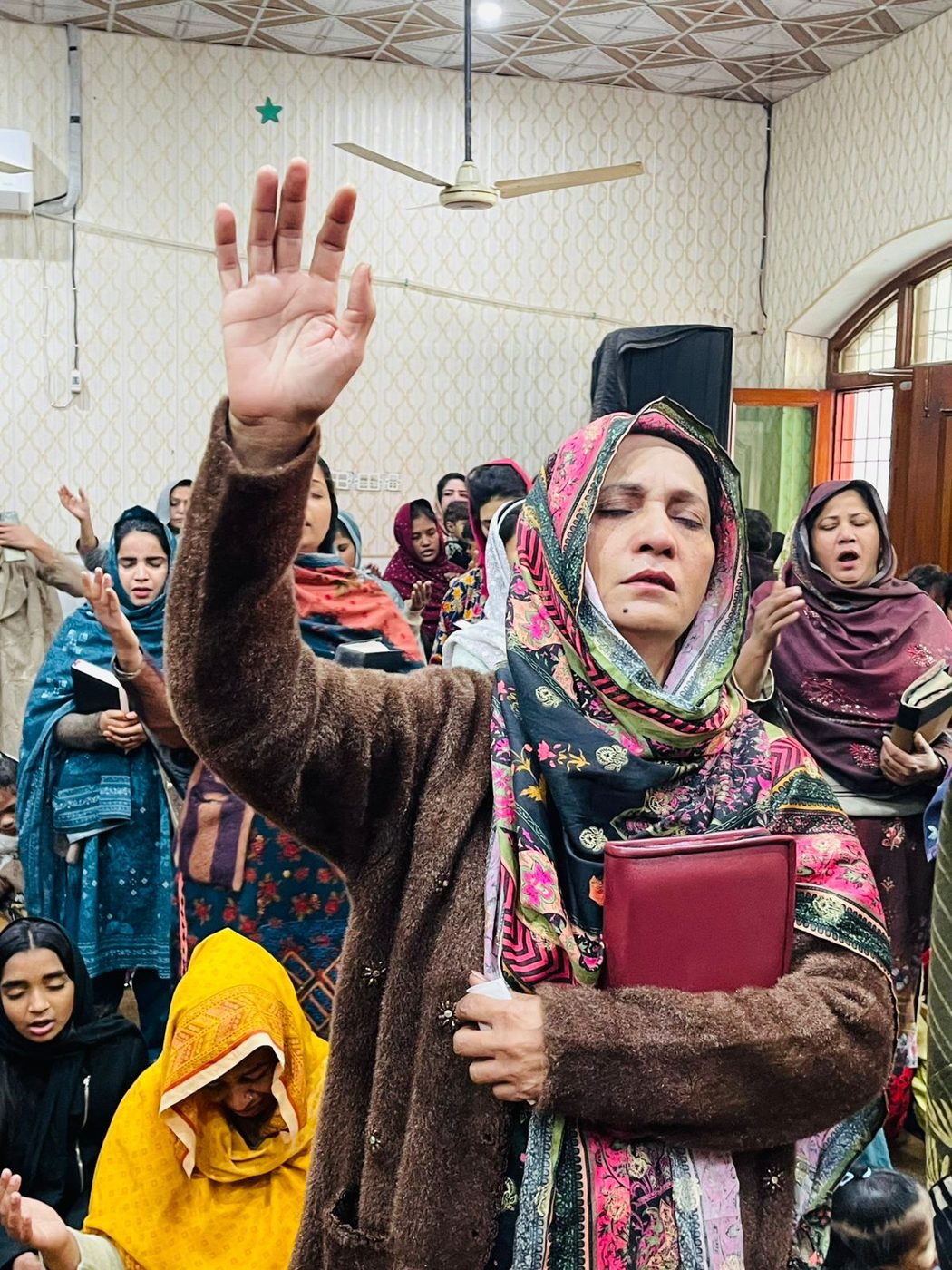 A woman lifting her hand in worship at John Paul's church in Pakistan